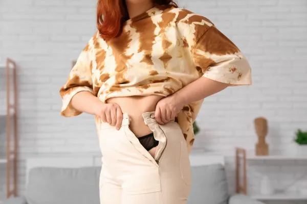 Image of woman trying to do her trousers up after pregnancy weight gain Bedford