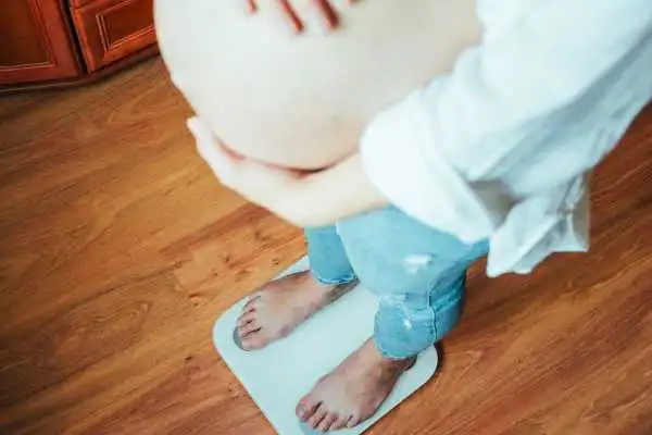 Image of woman weighing herself and experiencing weight gain through pregnancy Bedford